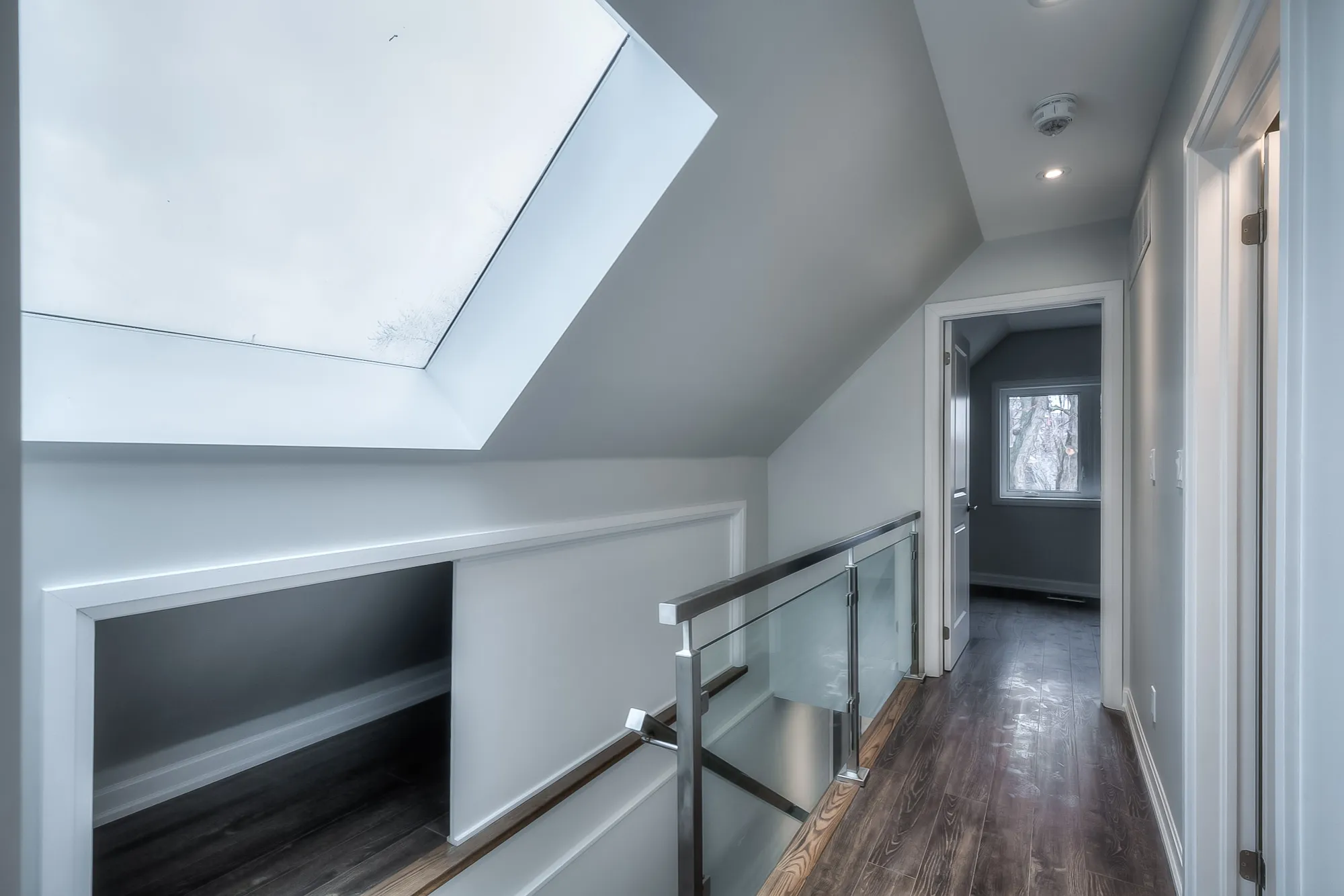 hallway with skylight, hardwood floors and staircase with glass and metal railing