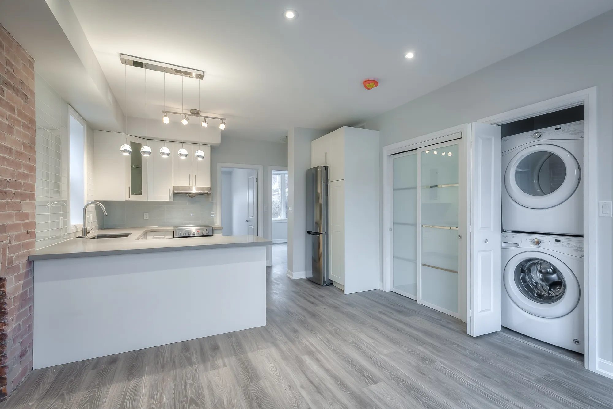 living room with exposed brick wall and hardwood floors with laundry machines in closet