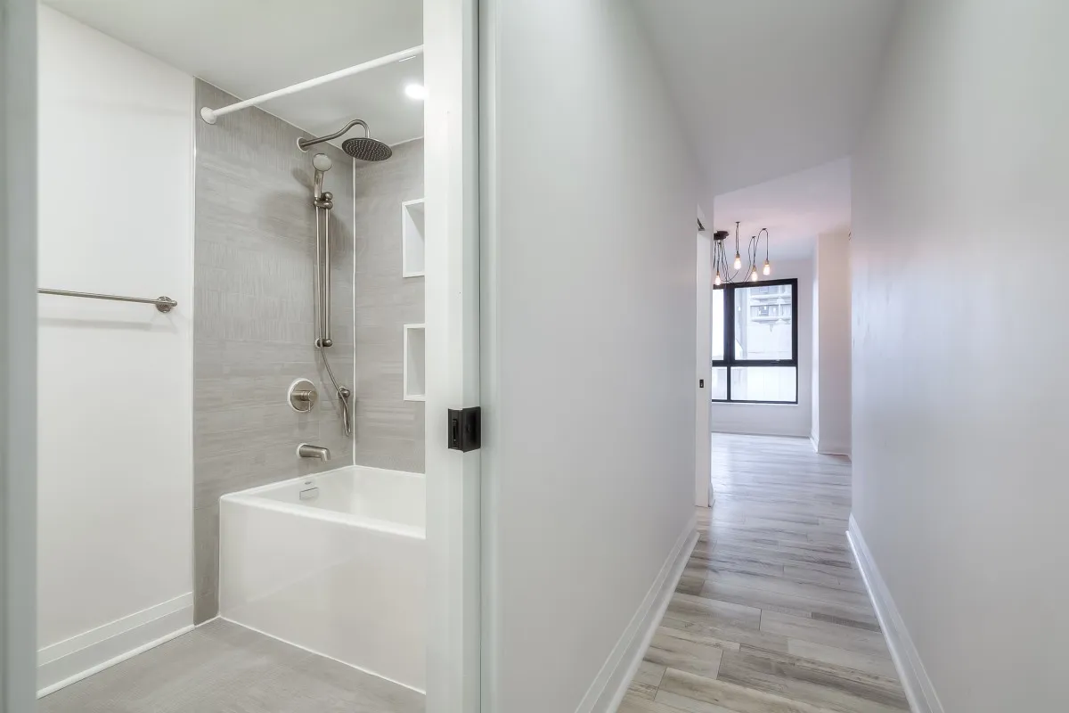 A bathroom with a shower and tub beside a hallway