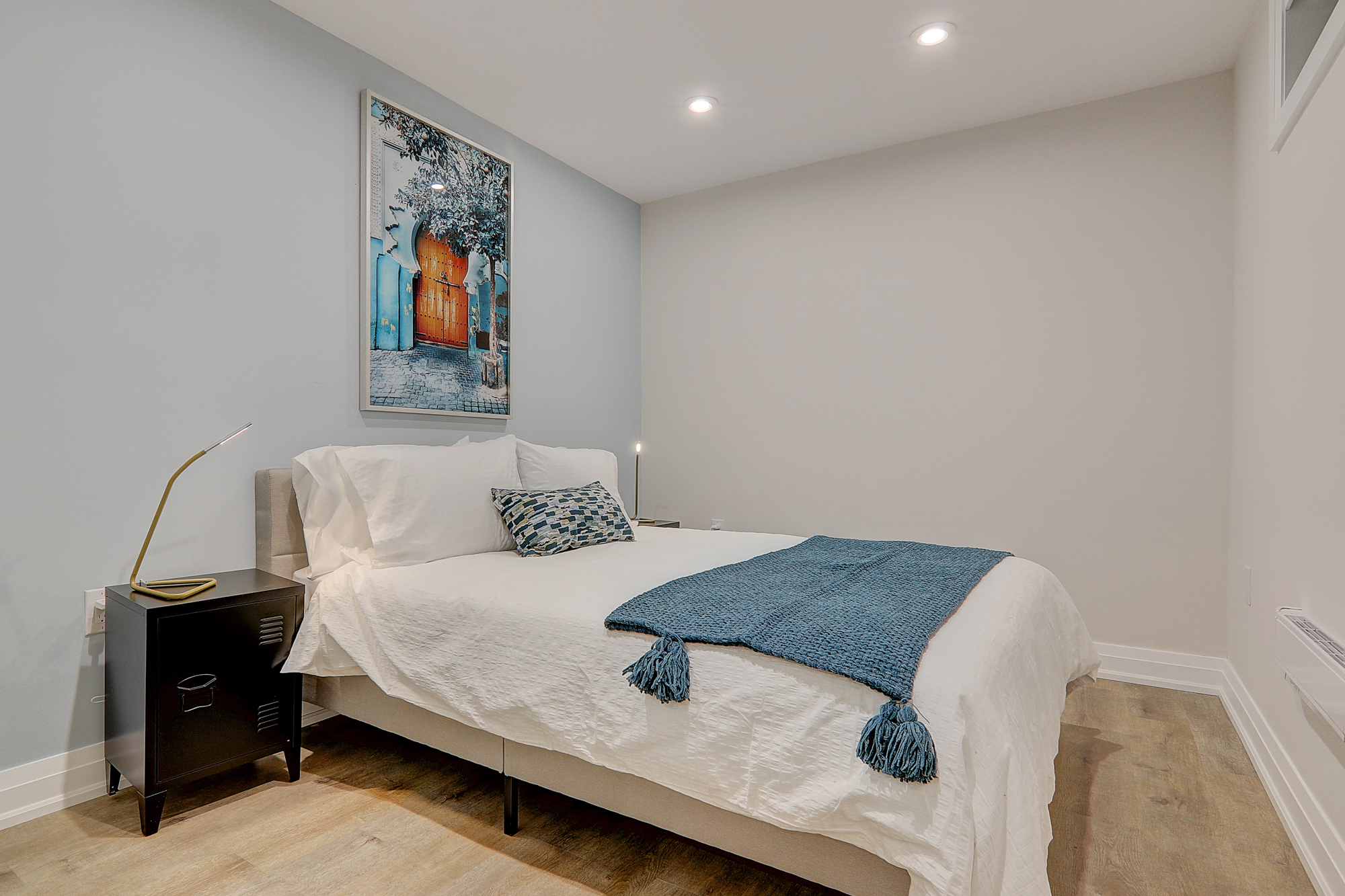 A bed with a blue blanket and a painting on the wall